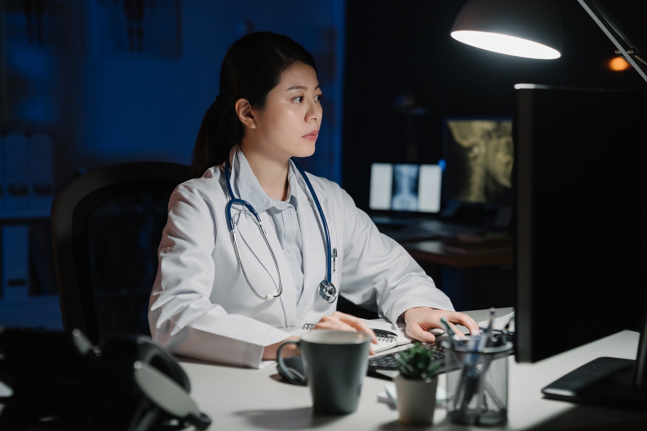A doctor reviews patient records on a computer at night