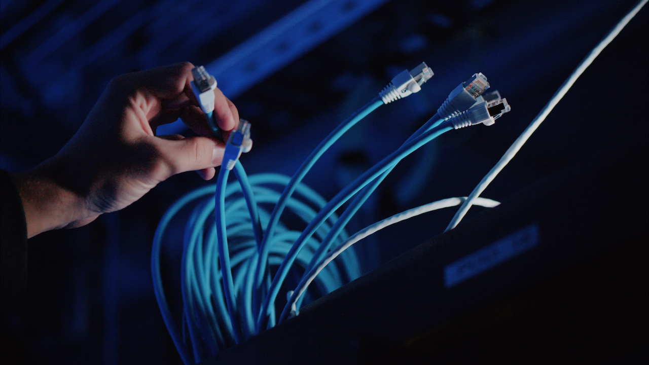 An engineer works on network cabling in blue light