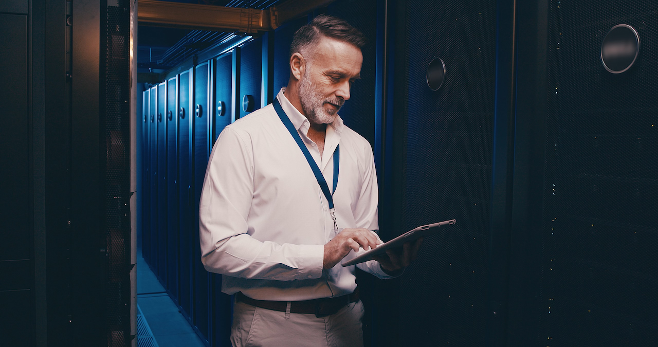 An engineer with a tablet in a server room aisle