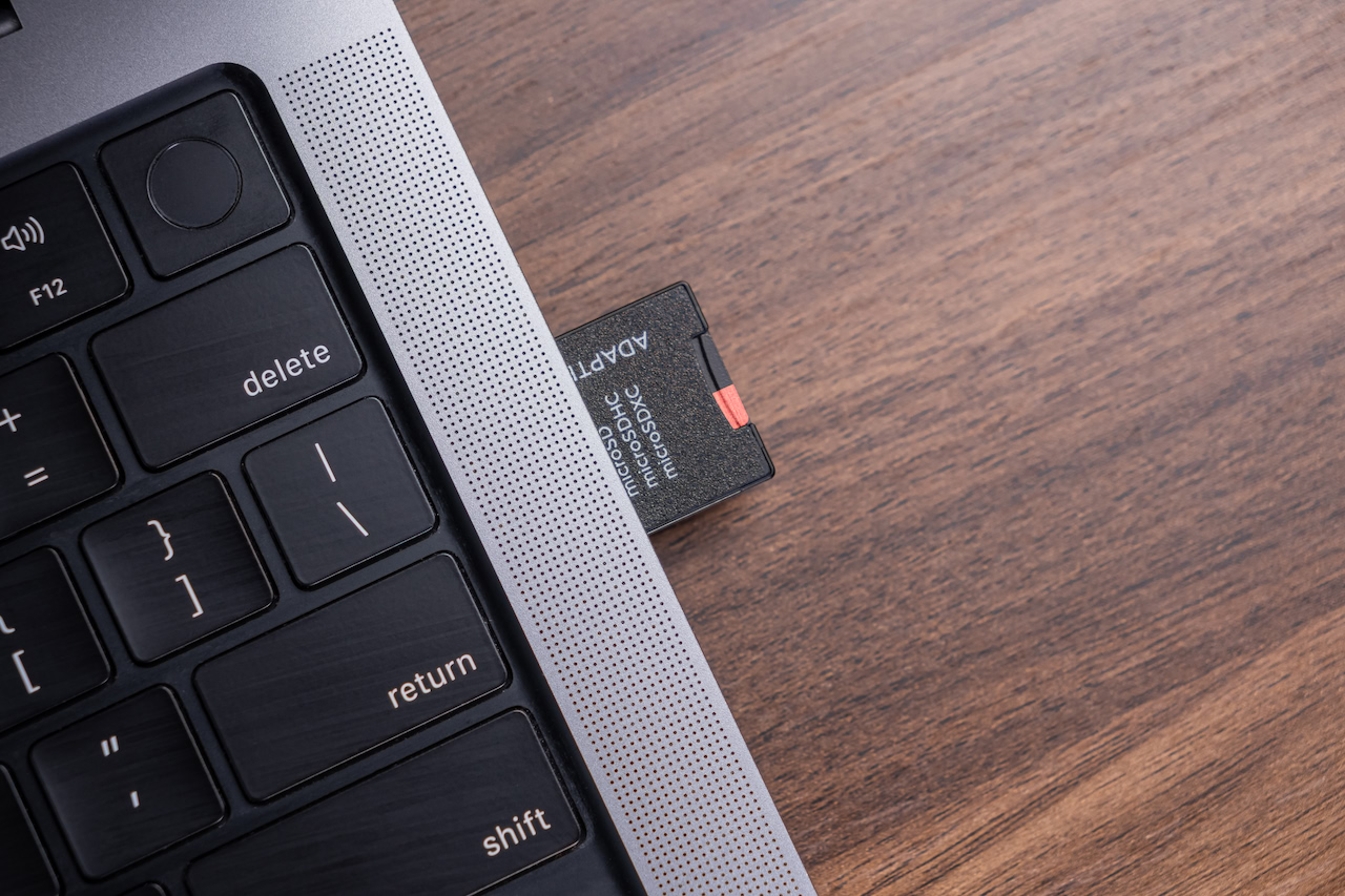 A memory card in the slot of a laptop on a wooden desk