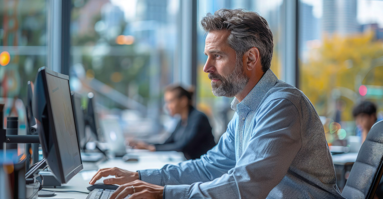 A man working at a computer by the window of an open-plan office
